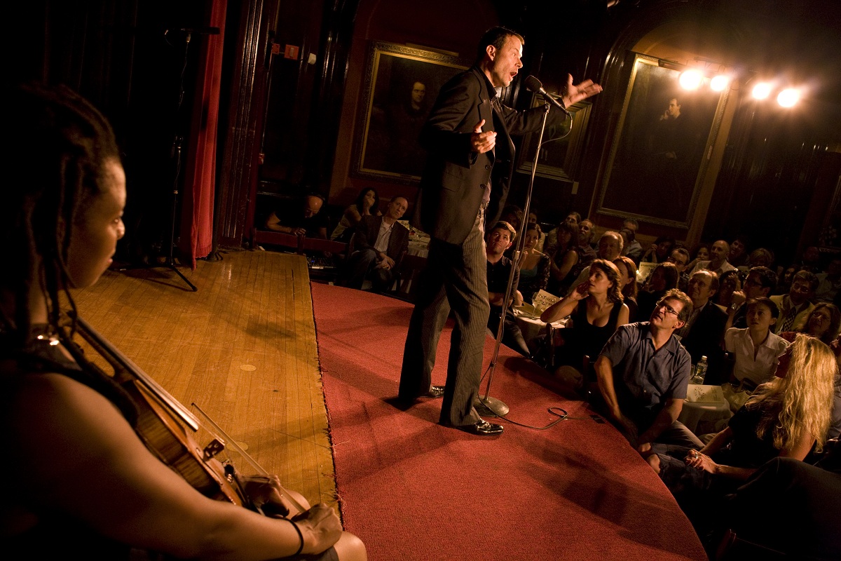 Man telling a story from The Moth mainstage. The room is full of people entranced by the speaker.