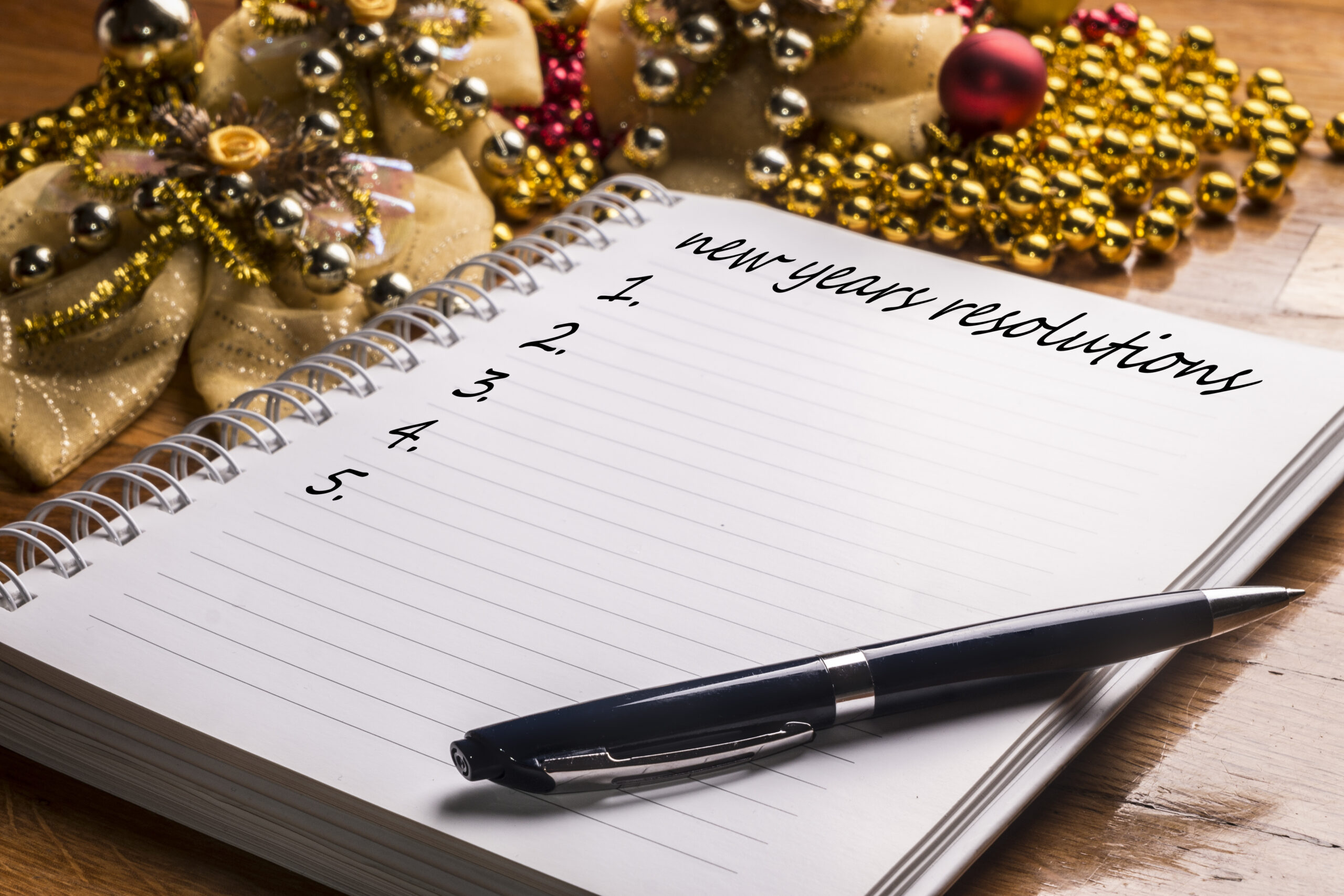 A photo of a notepad on a table with gold beads. It reads "New Years Resolution"