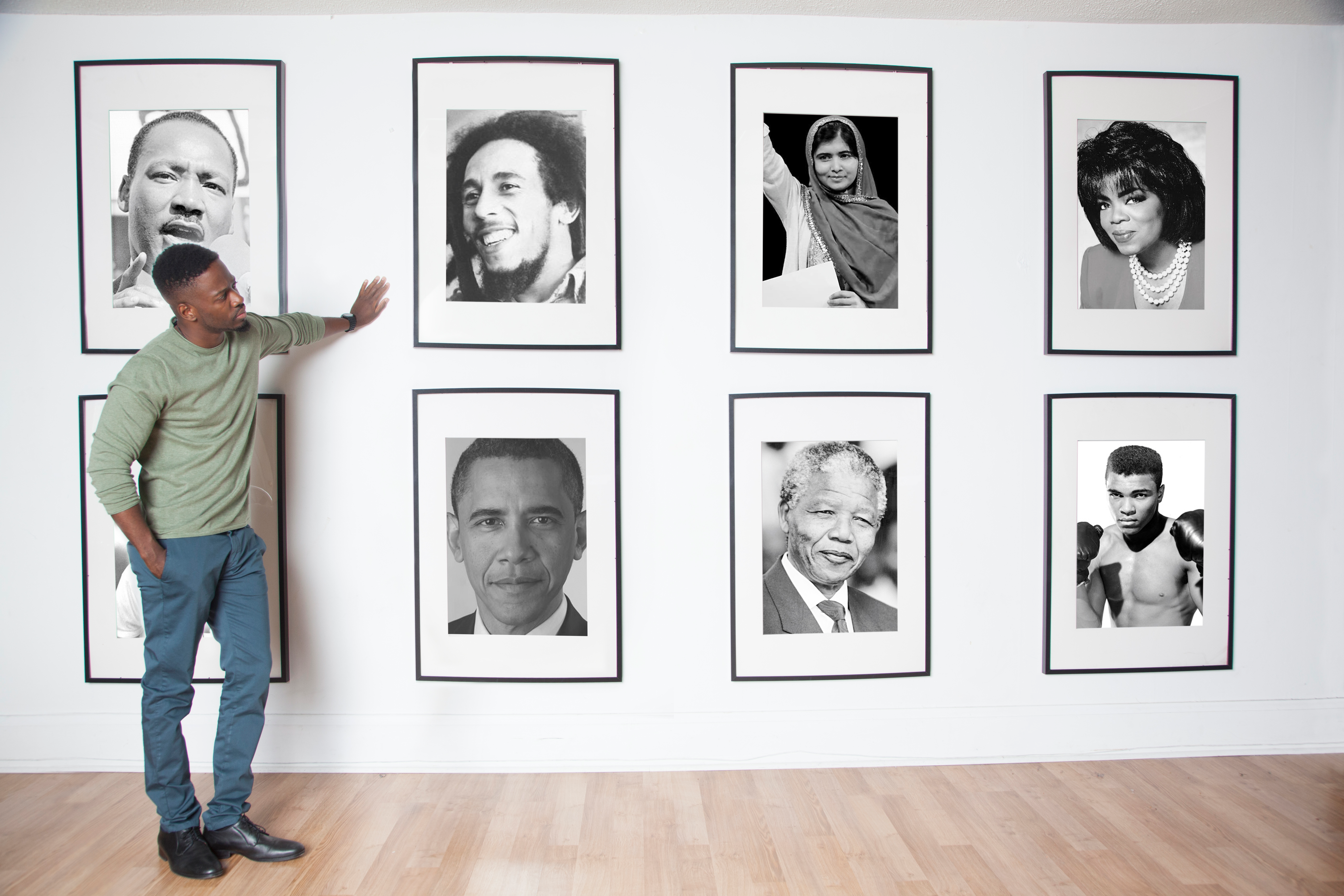 Shawn Boothe leaning on a wall of black and white photographs of famous people like Bob Marley and Oprha Winifrey.