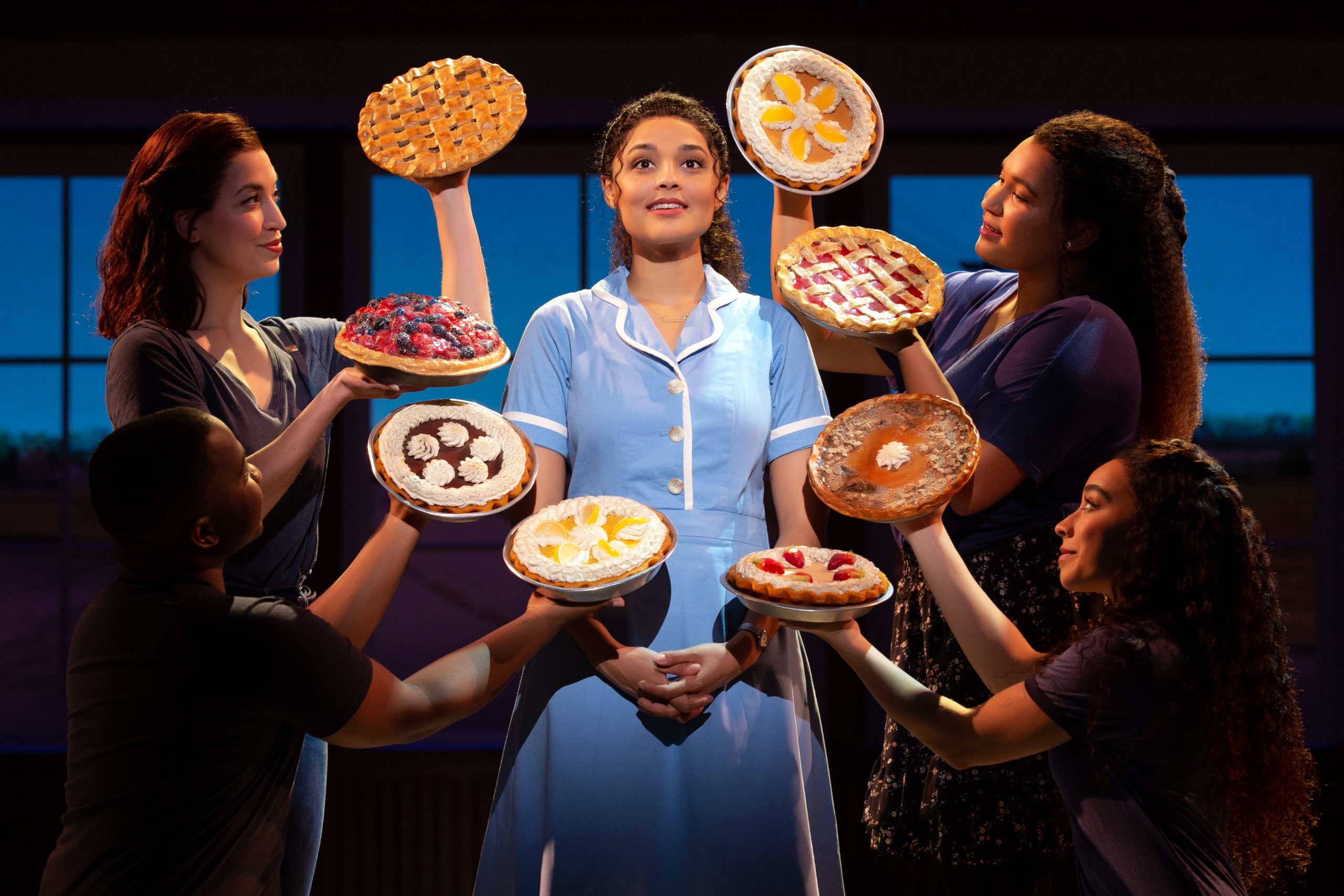 Jenna from the musical Waitress smiling surrounded by pies.