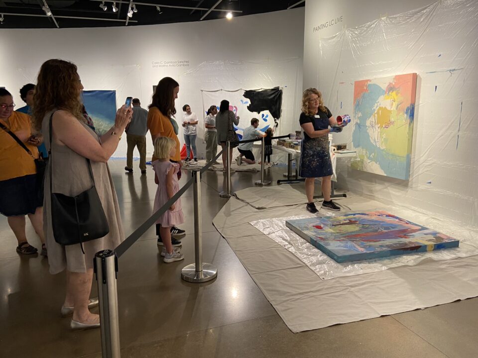 Jennifer Ivanovic Demonstrates her paint pouring technique to several people in the art gallery.